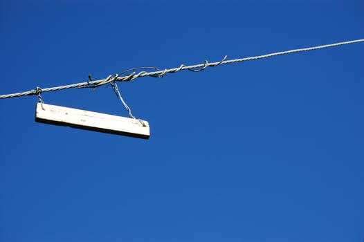 Plain white sign hung on a twisted metal cable against a blue sky