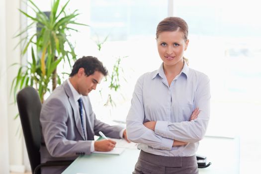 Young tradeswoman with arms folded and colleague sitting behind her