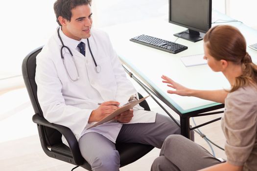 Young doctor writing down the symptoms his patient is describing