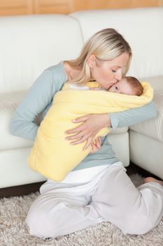 Affectionate young mom kissing her baby that is wrapped into a cover