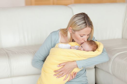 Lovely young mother kissing her baby which is wrapped into a cover
