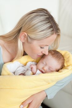 Affectionate young mother kissing her sleeping baby in her arms