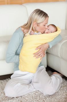 Young mom kissing her baby that is wrapped into a cover