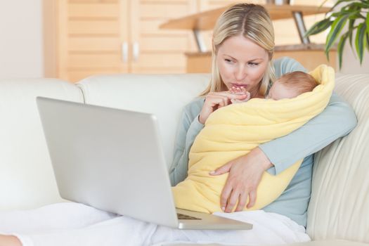 Young mother holding her baby while looking at her laptop