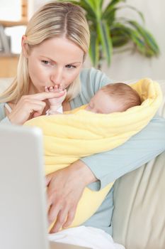 Young mother kissing her baby's hand while looking at the laptop