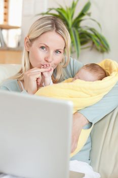 Young mother kissing her baby's hand while sitting on the sofa