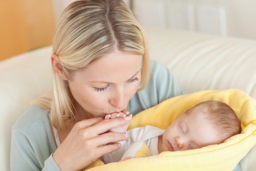 Young mother on the sofa kissing her baby's hand