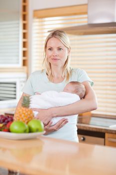 Young woman standing in the kitchen with her baby on her arms