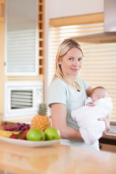 Side view of woman standing in the kitchen with her baby on her arms