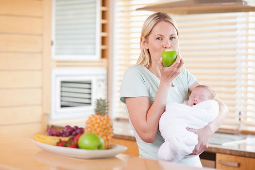 Young woman enjoying an apple with her baby on her arms