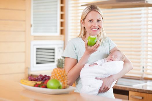 Smiling young woman with an apple and her baby on her arms