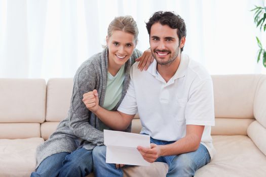Delighted couple reading a letter in their living room