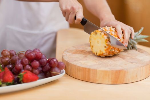 Close up of young feminine hands slicing a pineapple in her kitchen