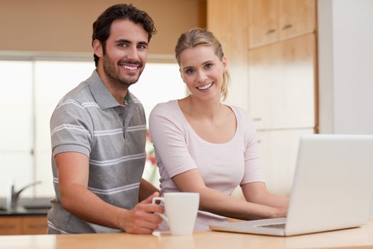 Smiling couple using a notebook while having coffee in their kitchen