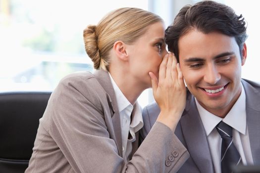 Young businesswoman whispering something to her colleague in a meeting room