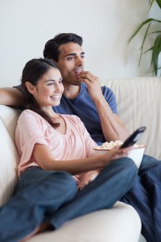 Portrait of a couple watching TV while eating popcorn in their living room
