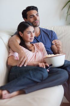 Portrait of a couple watching television while eating popcorn in their living room