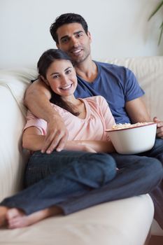 Portrait of a smiling couple watching television while eating popcorn in their living room