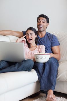 Portrait of a laughing couple watching a movie while eating popcorn with a laptop