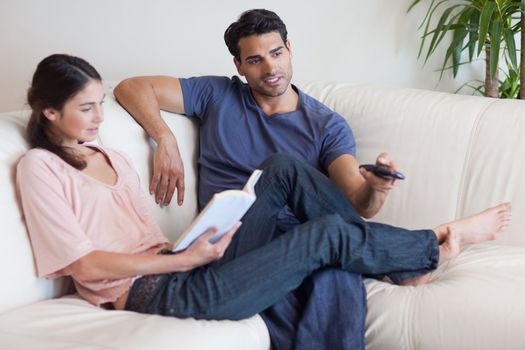 Woman reading a book while her fiance is watching television in their living room
