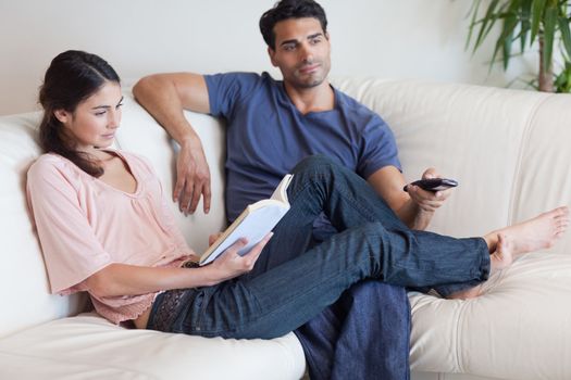 Woman reading a book while her fiance is watching TV in their living room