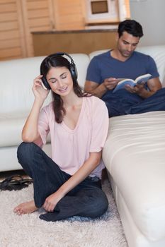 Portrait of a woman listening to music while her fiance is reading a book in their living room