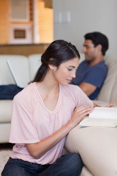 Portrait of a woman reading a book while her husband is using a laptop in their living room