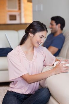 Portrait of a woman reading a book while her boyfriend is using a laptop in their living room