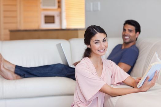 Woman reading a book while her boyfriend is using a laptop in their living room