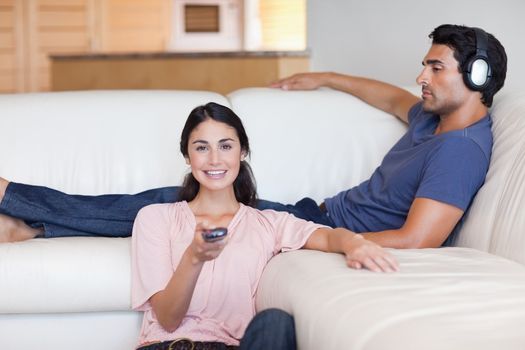 Woman watching television while her husband is listening to music in their living room