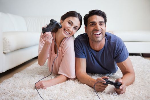 Delighted couple playing video games while lying on a carpet