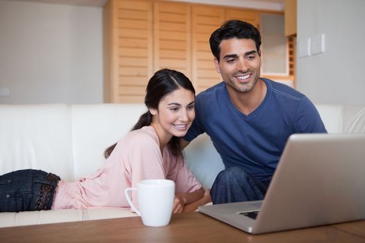 Young couple using a laptop while having a tea in their living room