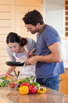 Portrait of a young couple cooking with a pan in their kitchen