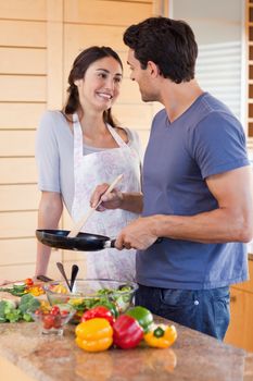 Portrait of a beautiful couple cooking with a pan in their kitchen