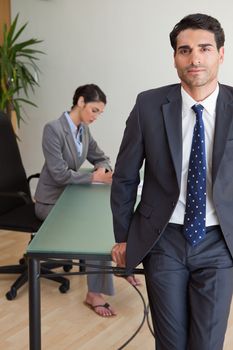 Portrait of a businessman posing while his colleague is working in an office