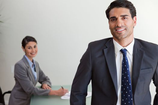 Good looking businessman posing while his colleague is working in an office