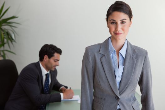 Beautiful businesswoman posing while her colleague is working in an office
