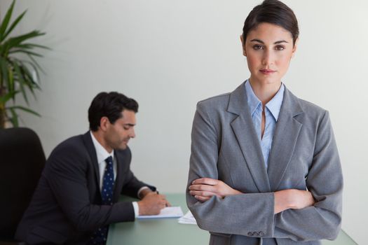 Professional businesswoman posing while her colleague is working in an office