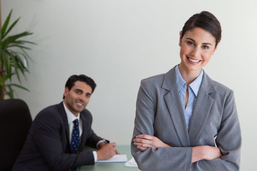 Happy businesswoman posing while her colleague is working in an office