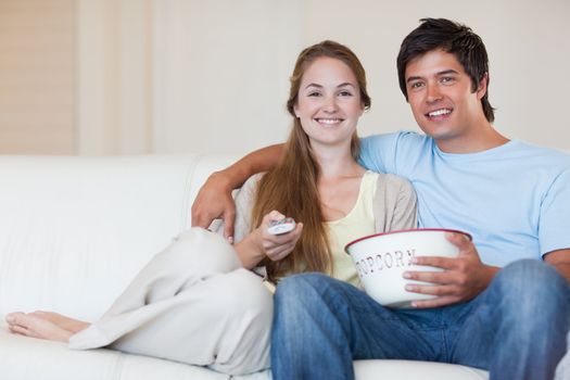 Young couple watching television while eating popcorn in their living room