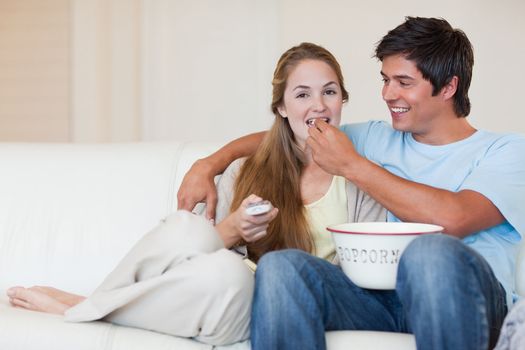 Happy couple watching television while eating popcorn in their living room