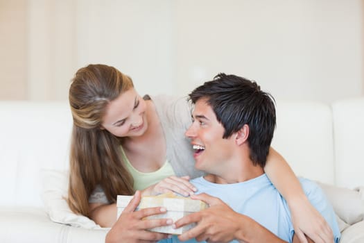 Woman offering a present to her boyfriend in their living room