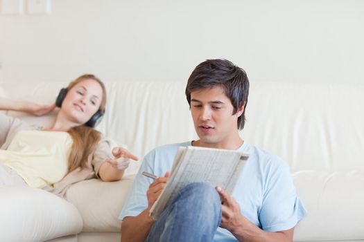 Woman helping her fiance to do crosswords while listening to music in their living room