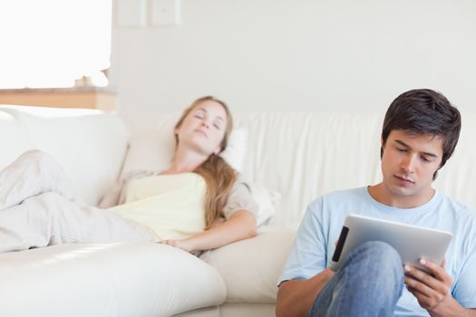 Man using a tablet computer while his girlfriend is sleeping in their living room