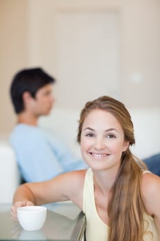 Portrait of a woman having a coffee while her husband is sitting on a sofa in their living room