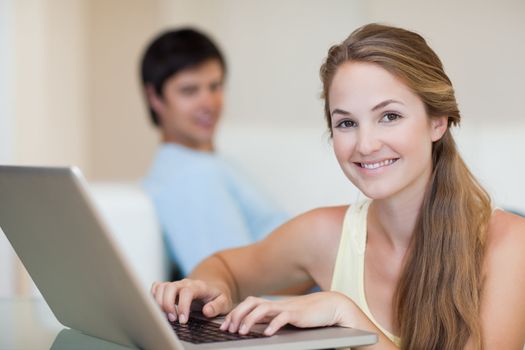 Woman using a laptop while her husband is sitting on a couch in their living room