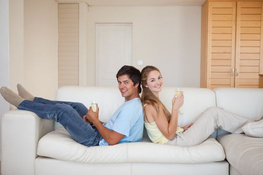 Couple sitting back to back while drinking sparkling wine in their living room