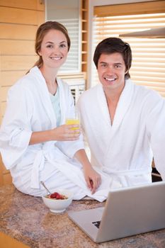 Portrait of a charming couple having breakfast while using a notebook in their kitchen