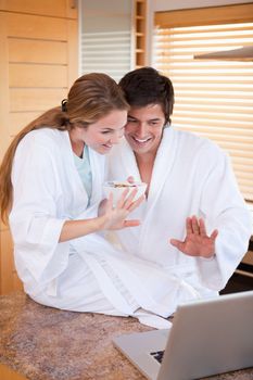 Portrait of a couple having breakfast while waving at their laptop in their kitchen