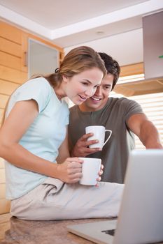 Portrait of a young couple having tea while using a laptop in their kitchen